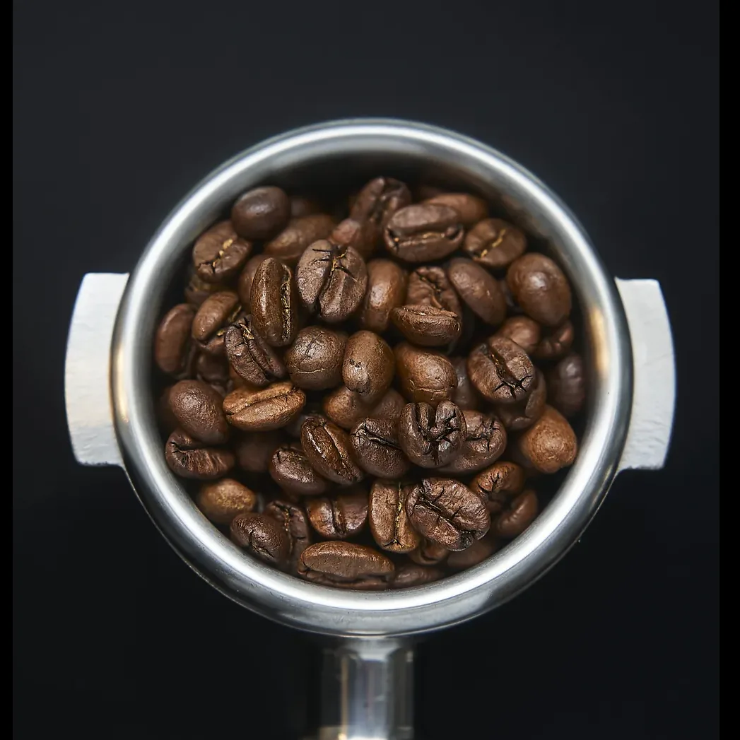 Siebträger von oben, gefüllt mit ganzen Kaffeebohnen, auf schwarzem Grund